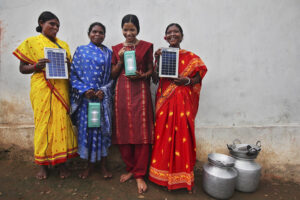 Fire kvinner kledd i sari viser fram solcellepanel og lykter