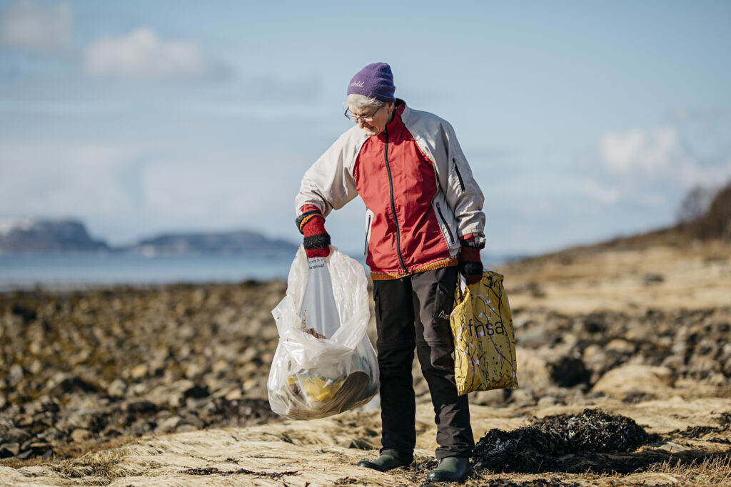 Eldre kvinne rydder søppel på stranda