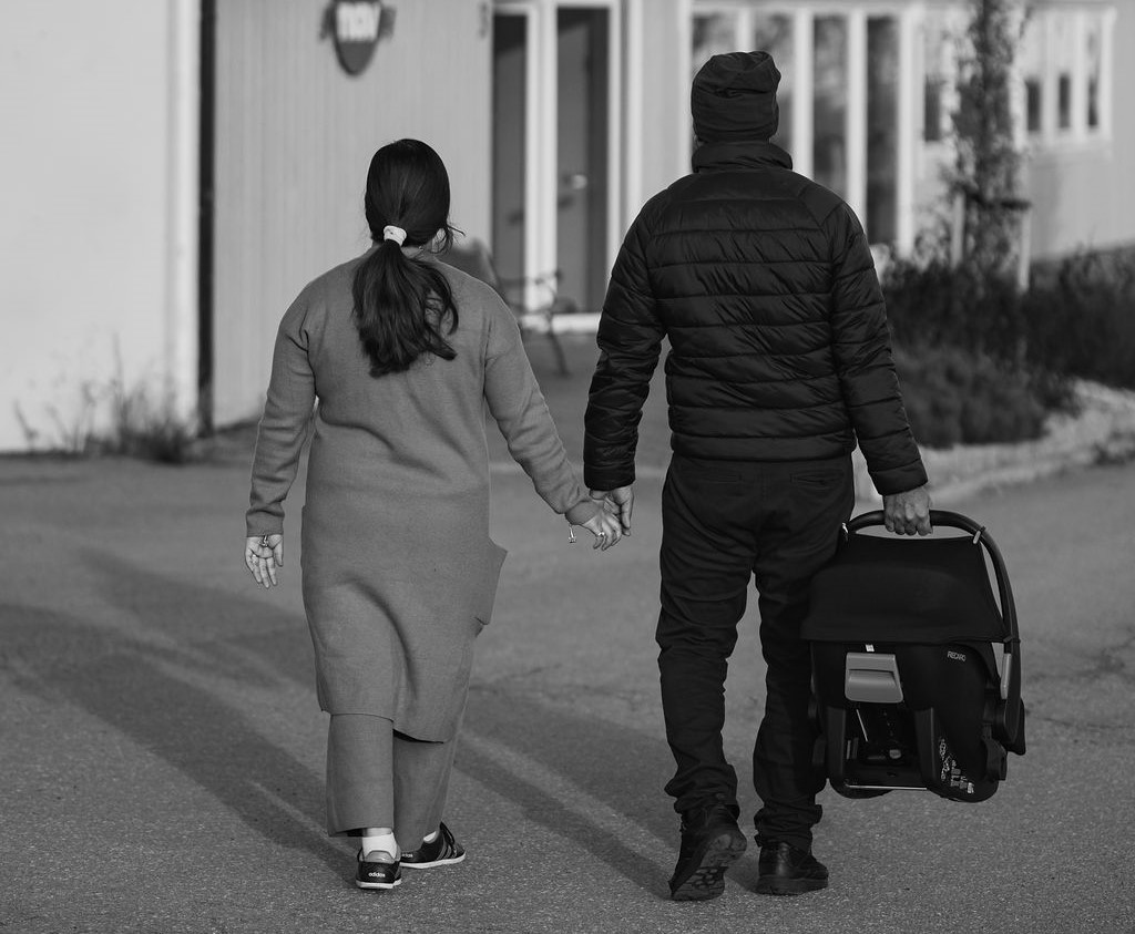 To foreldre med baby i bilstol går mot inngangen til NAV