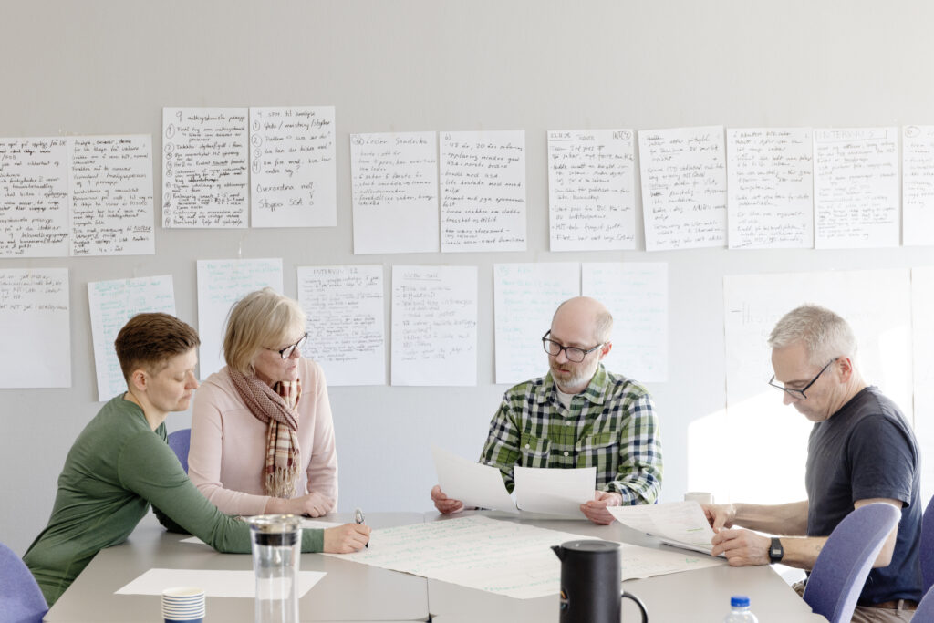 Kollegar på Nordlandsforskning sit ved eit gruppebord og arbeider med datagjennomgang under workshop i kollektiv kvalitativ analyse.